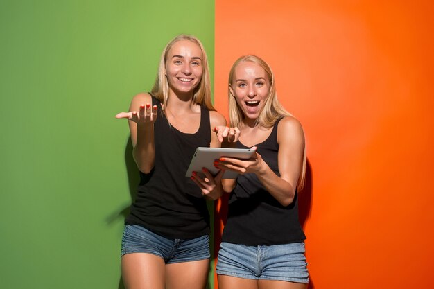 Bild von zwei jungen glücklichen Frauen, die die Kamera betrachten und Laptops im Studio halten.