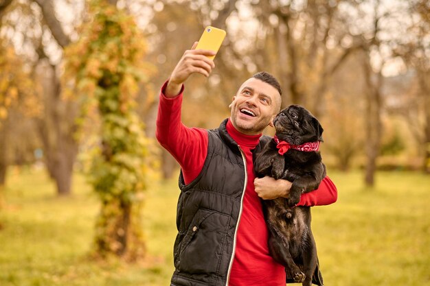 Bilder machen. Ein Mann mit seinem Hund in den Händen macht Selfie