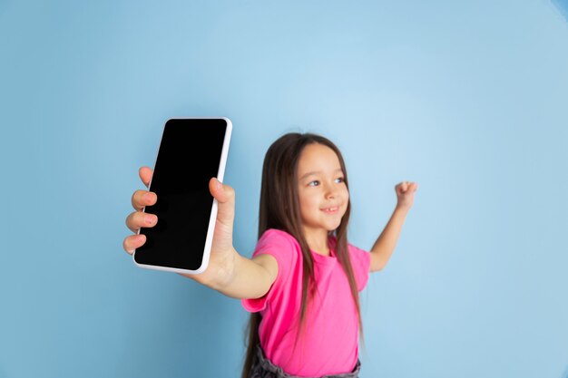 Bildschirm des Telefons anzeigen. Kaukasisches Porträt des kleinen Mädchens auf blauer Wand.