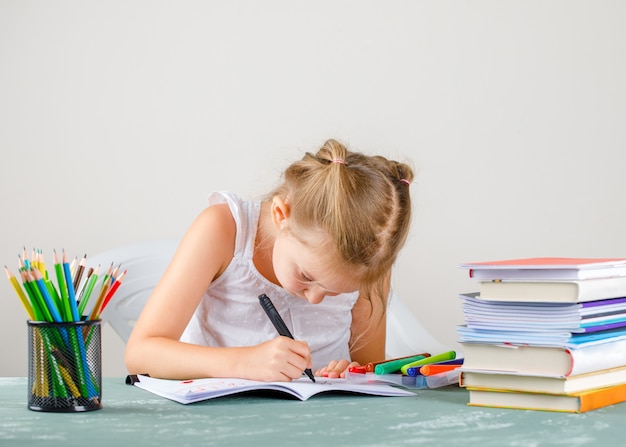 Bildungskonzept mit Seitenansicht des Schulbedarfs. kleines Mädchen, das auf Heft zeichnet.