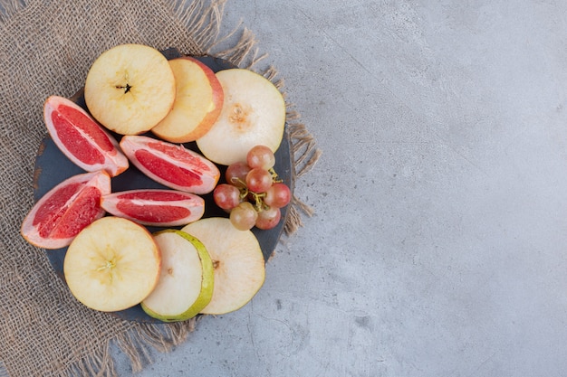 Birnen- und Grapefruitscheiben mit einer kleinen Weintraube auf einem Holzbrett auf Marmorhintergrund.