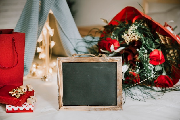 Blackboard in der Nähe von Blumen und Geschenkboxen