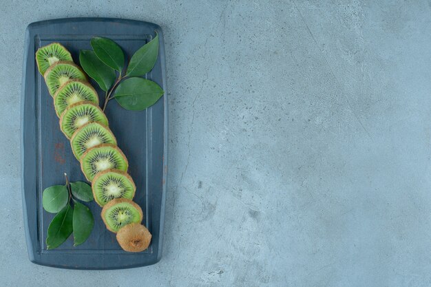 Blätter und geschnittene Kiwi auf einem Holztablett, auf dem Marmorhintergrund.