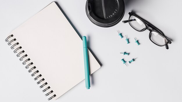 Blank Spiralblock; Stift; Kaffeetasse; Brillen und Pins auf weißem Hintergrund