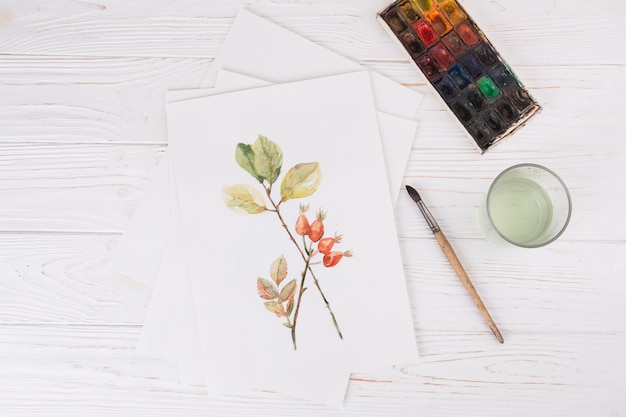 Blatt mit Pflanzenfarbe in der Nähe von Glas, Pinsel und Wasserfarben