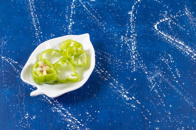 Blattförmiger Teller mit grünen Paprikaringen auf Marmoroberfläche
