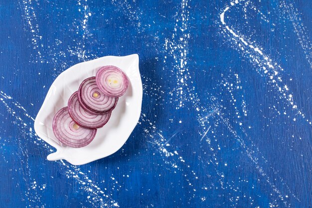 Blattförmiger Teller mit violetten Zwiebelringen auf Marmoroberfläche