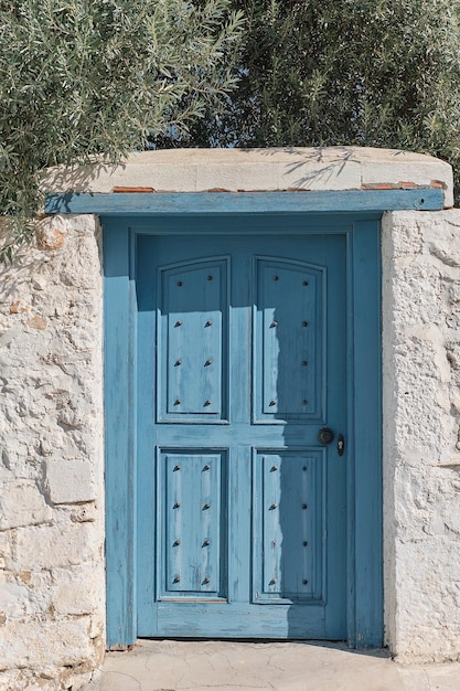 Kostenloses Foto blaue alte tür an der steinweißen wand des hauses olivenzweige hängen über der tür vertikaler rahmen mittelmeerküste antiker vintage-stil griechenland reisezeit hintergrundidee