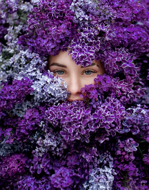 Blaue Augen des jungen kaukasischen Mädchens, umgeben von viel violettem Flieder, Tapete