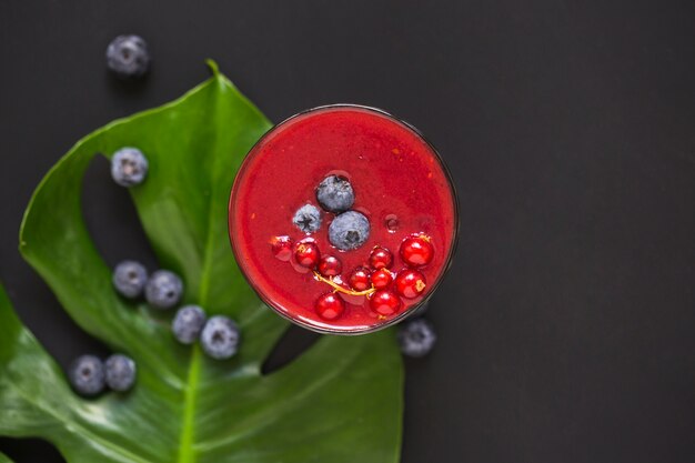 Blaue Beeren auf Smoothie und grünem Blatt gegen schwarzen Hintergrund