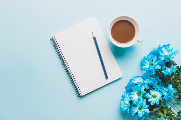 Blaue Blumen in der Nähe von Kaffee und Notebook