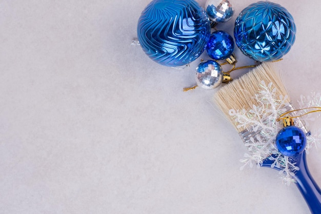 Blaue Bürste mit Weihnachtskugeln auf weißem Tisch.