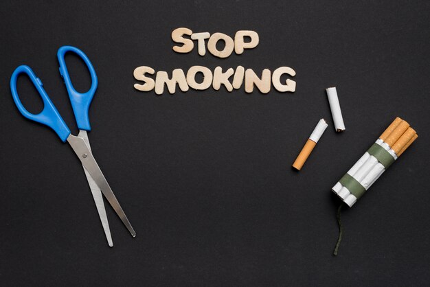 Blaue Schere mit aufhören, Text und Zigarette auf schwarzem Hintergrund zu rauchen