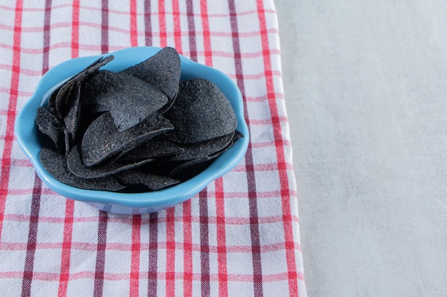 Blaue Schüssel mit knusprigen schwarzen Chips und Tischdecke auf Stein.