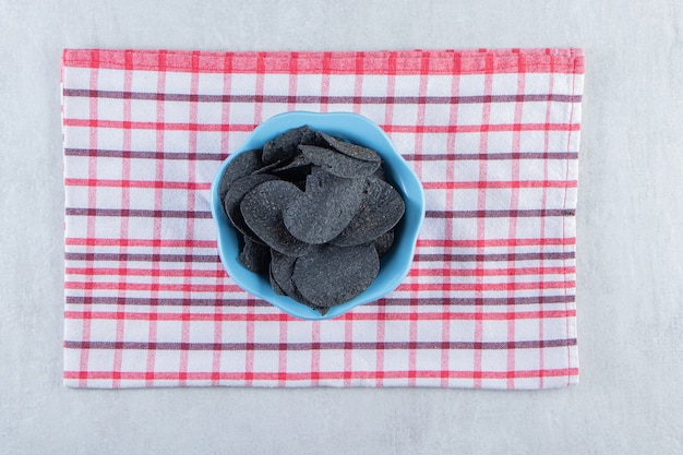 Kostenloses Foto blaue schüssel mit knusprigen schwarzen chips und tischdecke auf stein.