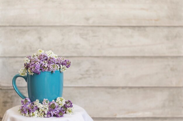 Blauer Becher mit dekorativen Blumen und Holzuntergrund