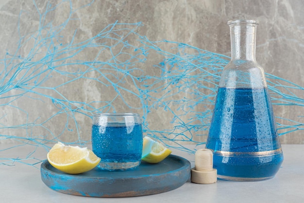 Blauer Cocktail in Glas und Flasche mit Zitronenscheiben auf blauem Teller