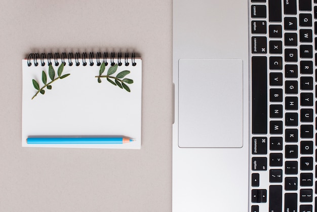 Kostenloses Foto blauer farbiger bleistift auf gewundenem notizblock und laptop auf grauem hintergrund