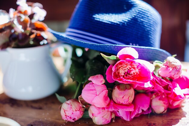 Blauer Hut liegt auf einem Blumenstrauß von rosa Pfingstrosen