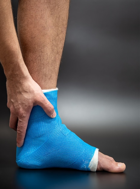 Blauer Knöchel der Schiene. Verbundenes Bein warf auf männlichen Patienten auf dunklem unscharfem Hintergrund. Sportverletzungskonzept.