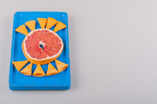 Blauer Teller mit Dreieckschips und Grapefruitscheibe auf weißem Hintergrund. Foto in hoher Qualität