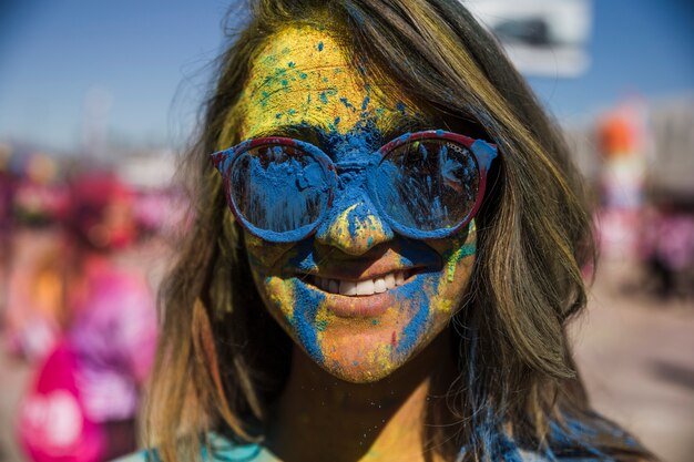 Blaues und gelbes holi Farbpulver auf dem Gesicht der Frau