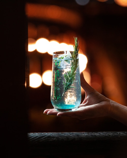 Blaues weißes Alkoholgetränk mit einer Niederlassung des Rosmarins in der Hand.