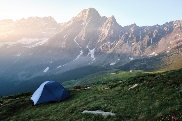 blaues Zelt auf einem grasbewachsenen Hügel mit Bergen und klarem Himmel
