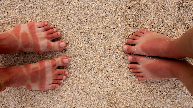 Kostenloses Foto blick auf die sonnenbrandfüße einer frau und eines kindes vom tragen von sandalen am strand