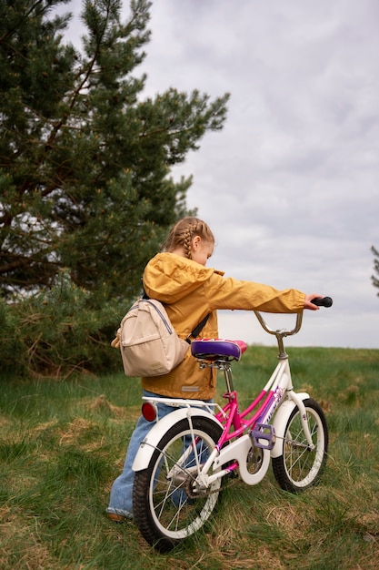 Blick auf ein kleines Mädchen mit Rucksack und Fahrrad, das in der Natur unterwegs ist