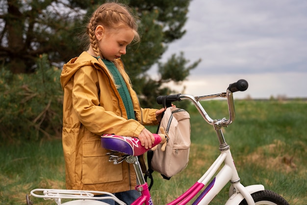 Blick auf ein kleines Mädchen mit Rucksack und Fahrrad, das in der Natur unterwegs ist