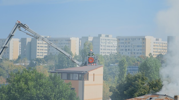 Blick auf Feuerwehrleute, die einen Plattformwagen der Feuerwehr verwenden, um das Feuer aus einem brennenden Gebäude im Stadtviertel zu löschen. Feuerwehrleute mit Wasser versuchen, Flammen aus dem Haus zu löschen