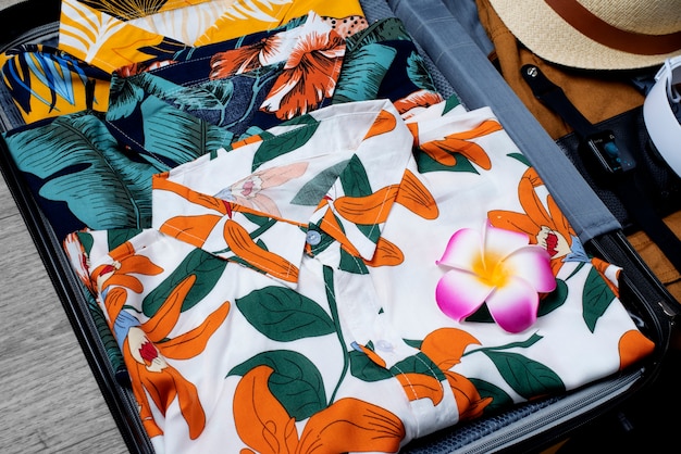 Blick auf hawaiianische Hemden, die im Gepäck mit Hut und Kopfhörern gestapelt sind