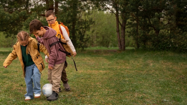 Kostenloses Foto blick auf kleine kinder mit rucksäcken, die in der natur ball spielen