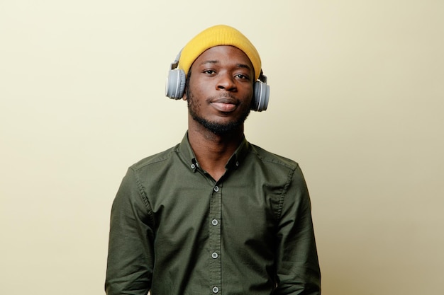 Blick in die Kamera junger afrikanisch-amerikanischer Mann mit Hut und Kopfhörern, der ein grünes Hemd auf weißem Hintergrund trägt