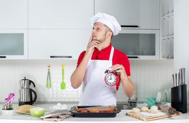 Blick von oben auf den jungen verträumten männlichen Koch, der eine Uhr in der weißen Küche hält