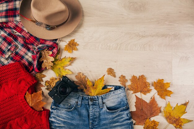 Blick von oben auf die flache Lage von Frauenstil und Accessoires, rotem Strickpullover, kariertem Flanellhemd, Jeans, Hut, Herbstmode-Trend, Vintage-Fotokamera, Traveller-Outfit