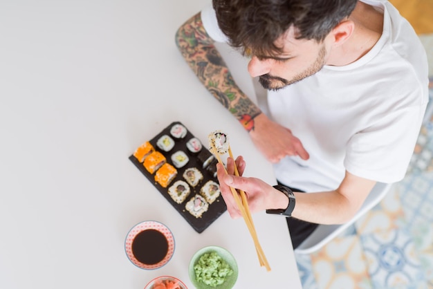 Blick von oben auf einen jungen Mann, der mit Stäbchen Sushi-asiatisches Essen isst