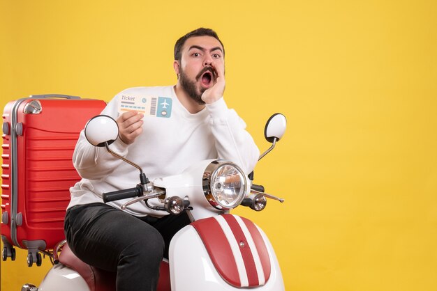 Blick von oben auf einen jungen reisenden Mann, der auf einem Motorrad sitzt, mit einem Koffer darauf, der ein Ticket hält