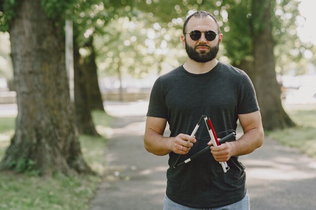 Blinder Mann. Menschen mit Behinderung, Behinderte und Alltag. Sehbehinderter Mann mit Spazierstock, absteigende Stufen im Stadtpark.