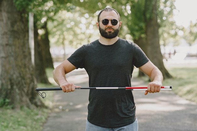 Blinder Mann. Menschen mit Behinderung, Behinderte und Alltag. Sehbehinderter Mann mit Spazierstock, absteigende Stufen im Stadtpark.