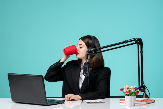 Blogger-Journalistin, brünettes süßes Mädchen im schwarzen Blazer, das Rede vor der Kamera beim Kaffeetrinken aufzeichnet