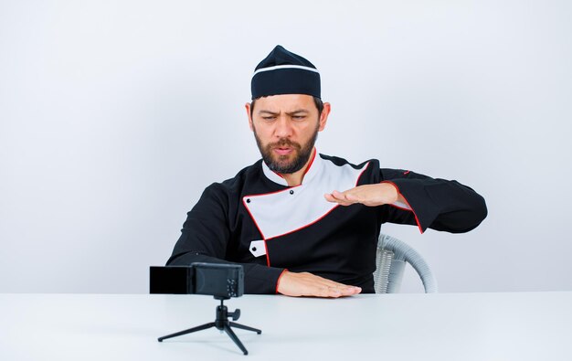 Blogger-Koch zeigt Größengeste, indem er vor seiner Minikamera auf weißem Hintergrund sitzt