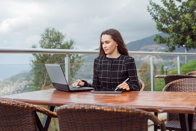 Blogger-Mädchen schaut auf den Laptop-Bildschirm, indem sie auf dem Hintergrund der Naturansicht sitzt