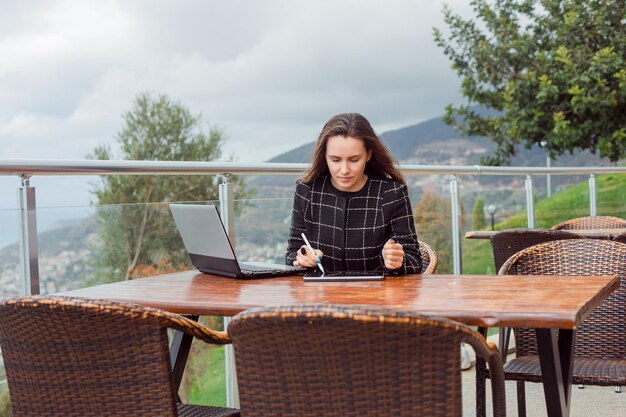 Blogger-Mädchen wacht auf dem Planshet-Computer auf, indem sie auf dem Hintergrund der Naturansicht sitzt