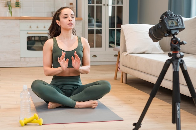 Bloggerin in Sportbekleidung, die auf Yogamatte sitzt