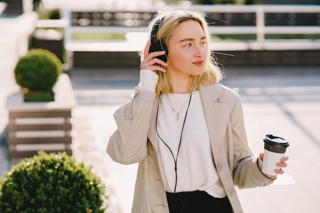 Blond geht in der Sommerstadt mit einer Tasse Kaffee spazieren