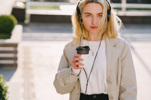 Blond geht in der Sommerstadt mit einer Tasse Kaffee spazieren
