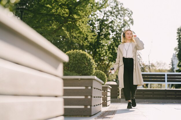 Blond geht in der Sommerstadt mit einer Tasse Kaffee spazieren