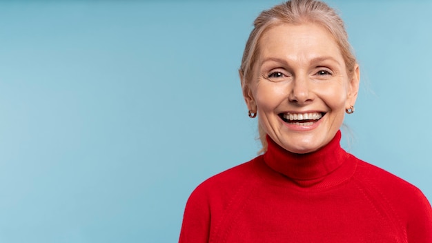 Blonde ältere Frau, die glücklich ist und gegen einen blauen Hintergrund lächelt
